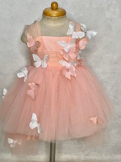 A close-up of our butterfly-themed dress in soft peach tulle. The 3D butterflies seem to flutter right off the dress, creating a truly enchanting look for a first birthday.
