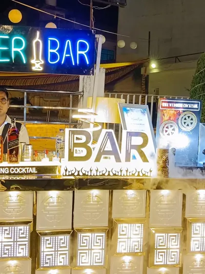 A bartender posing at a 'Shooter Bar' setup. The illuminated glass block front and multiple neon signs create a vibrant and exciting atmosphere.