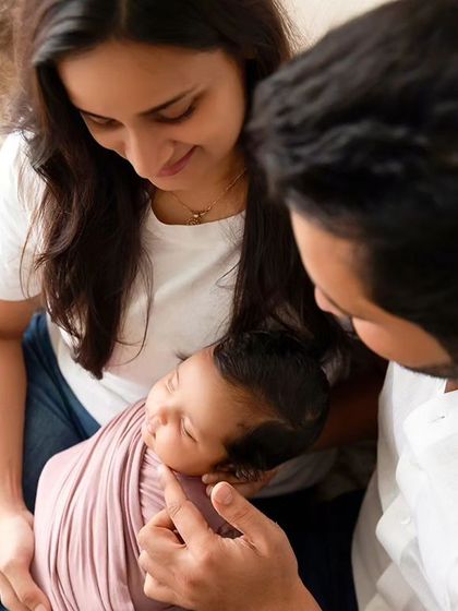 New parents gaze lovingly at their sleeping newborn, who is swaddled and held in their arms.
