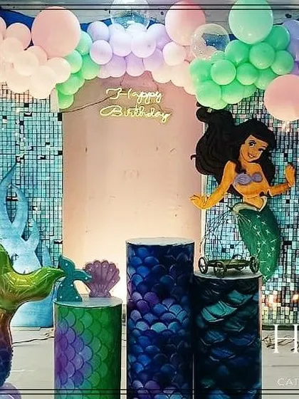 A magical mermaid-themed birthday party. This enchanting setup includes a shimmering backdrop, character cutouts of a mermaid, and custom-made props like a mermaid tail and coral reef elements to create an under-the-sea adventure.