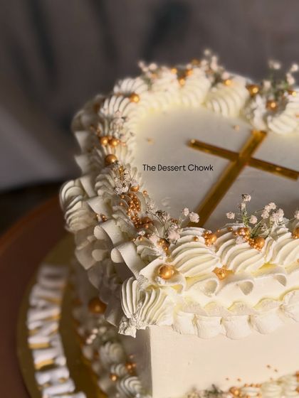 Another angle of the heart-shaped Confirmation cake, showing the golden cross and baby's breath flowers that complete the sacred theme.