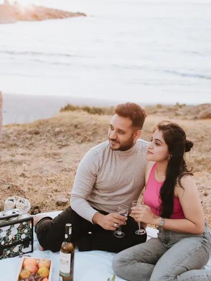 A cozy beach picnic scene from a pre-wedding shoot. The couple enjoys a glass of wine together, creating a relaxed and intimate setting with the ocean in the background.