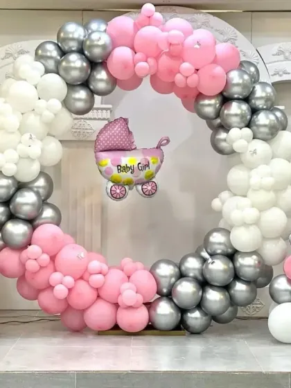 A lovely baby shower decoration for a girl. The circular balloon frame in pink, silver, and white is accented with baby girl and carriage foil balloons, perfect for celebrating the little one on the way.