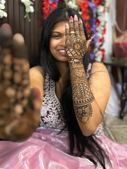 A playful pose from a bride showing off her henna. One hand displays the fresh, dark paste, while the other shows the intricate design on the back of the hand.