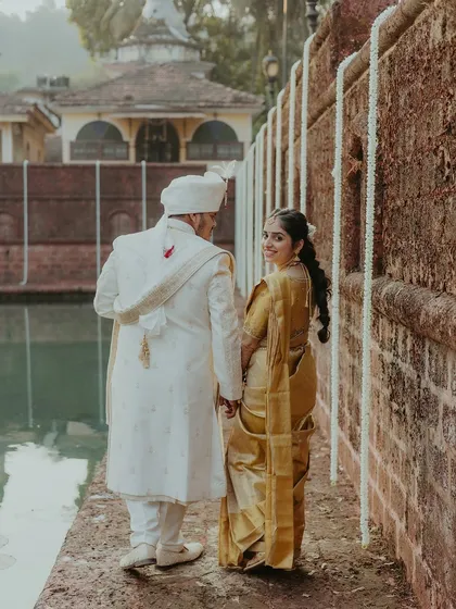 The couple walking hand-in-hand along a rustic stone wall, with the bride looking back at the camera with a smile.