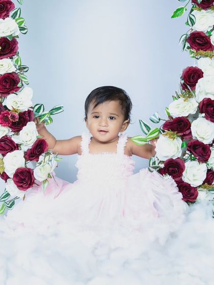 A beautiful portrait of a baby girl on a floral swing, surrounded by clouds.
