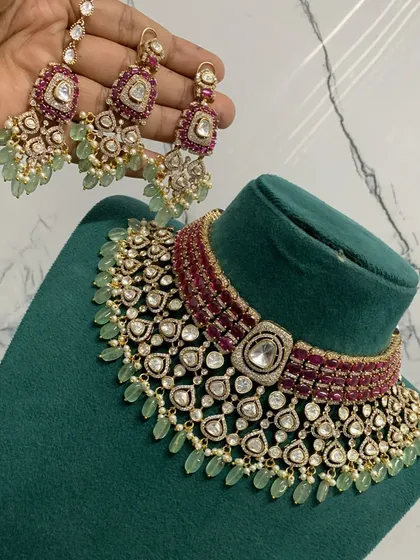 An exceptionally crafted bridal necklace set combining ruby-colored stones with mint-green bead drops. This piece demonstrates our ability to create complex, multi-colored designs with premium Moissanite stones for a rich, designer appeal.