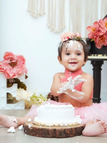 A happy baby covered in cake. We make sure to capture these priceless expressions during our fun-filled cake smash photoshoots.