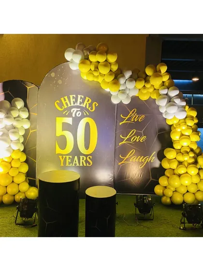 We celebrate major milestones with bold designs. This 50th birthday decoration features a custom-printed backdrop with "Cheers to 50 Years," framed by a yellow and white balloon arch for a festive and personalized touch.