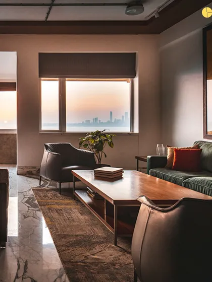 The living area of 'The Canvas' at dusk. The design balances the raw texture of the brick wall with the refined finish of the marble floor and the soft glow of the setting sun over the sea.