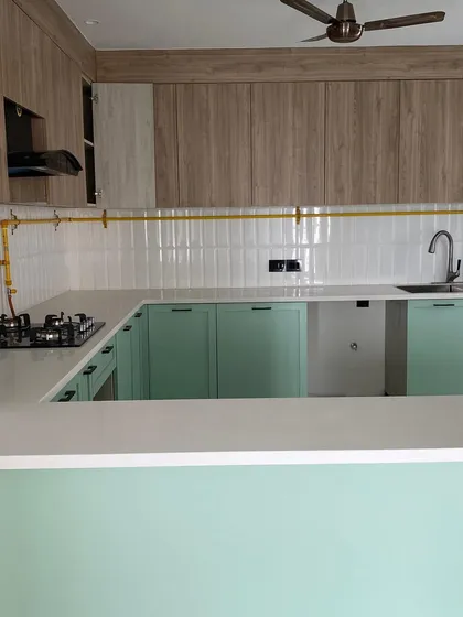 A fresh pistachio green and wood-themed kitchen, featuring a clean white countertop and modern subway tiles. The exposed brass gas pipe adds an industrial touch.