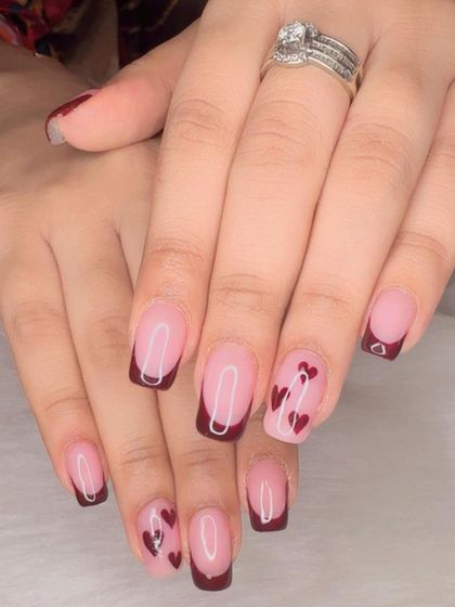 A romantic French manicure with deep red tips and accent nails featuring tiny painted hearts.