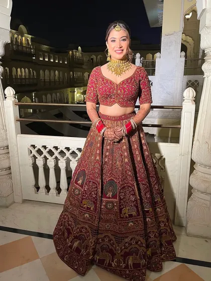 The bride in her full wedding attire. The floral updo I created for her adds a touch of romance that works beautifully with her traditional red lehenga in a palace setting.