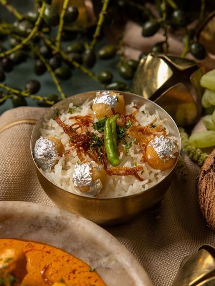 A close-up of our festive biryani, garnished with fried onions, fresh chili, and delicate silver leaf (vark).