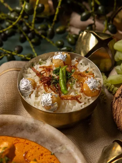 Our festive biryani from the 'RUMI' menu, served in a traditional brass bowl and garnished with fried onions, green chili, and silver leaf vark.
