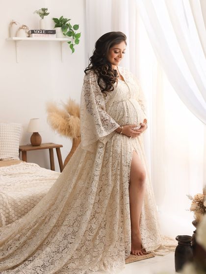 The light filtering through the window beautifully highlights the lace details of the gown and the serene expression of the mom-to-be in this classic boho maternity portrait.