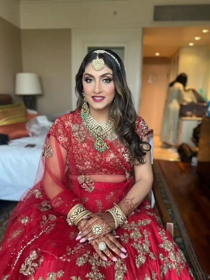 A beautiful bride seated and ready for her wedding. The red lehenga, a classic choice, is paired with glowing makeup and soft curls for a romantic feel.