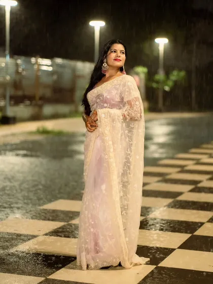 A full-length elegant pose. The checkerboard pattern of the ground contrasts beautifully with the soft, flowing saree.