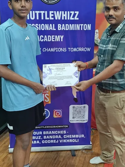 Recognizing perseverance and participation at our in-house badminton tournament. A coach presents a certificate to a young participant.