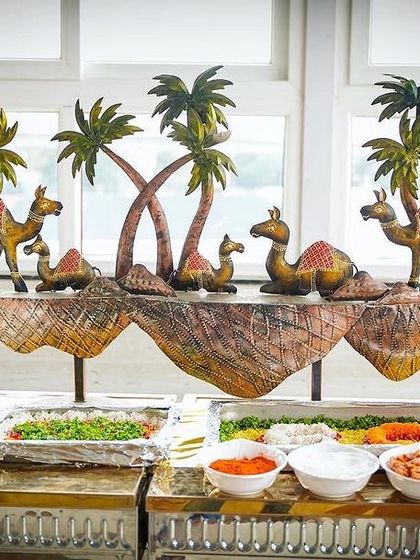 A desert-themed salad bar setup. The decorative camels and palm trees add a playful and creative touch to the food station, making even the salad course an interesting feature.