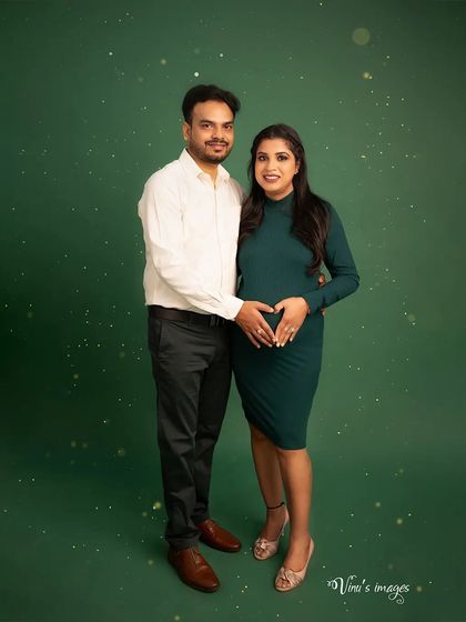 A classic couple's portrait against a clean green backdrop. The heart shape they make on the baby bump is a simple and beautiful expression of their love.