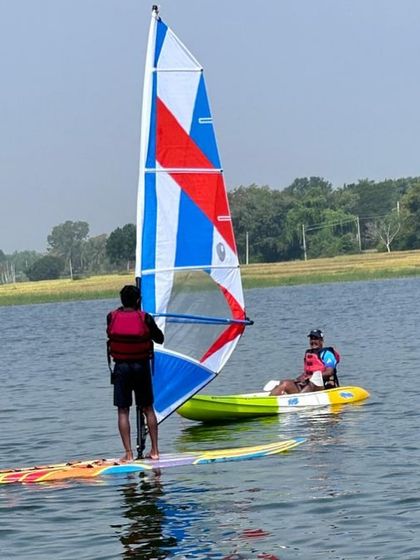 A participant learns to handle a windsurfing sail at our Ambigarahalli center, with a kayaker paddling nearby.