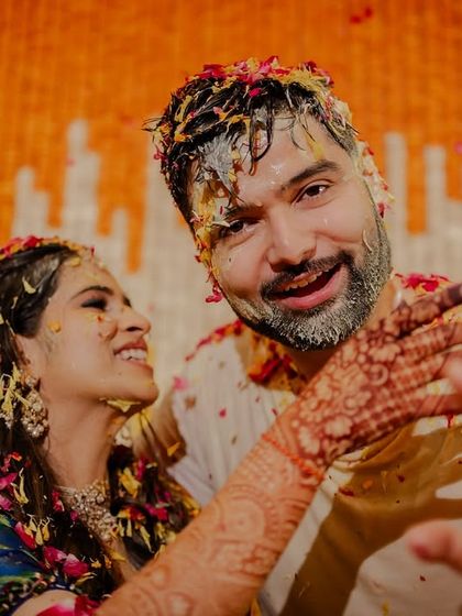 A candid shot of the couple playfully interacting mid-Haldi. Her mehndi-laden hand reaching out is a beautiful detail.