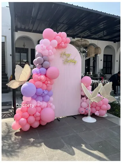 A simple yet elegant photo backdrop with a pink balloon garland and large, glowing butterfly props.