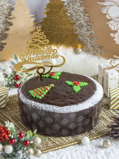 A traditional Christmas plum cake with simple, festive decorations and a "Merry Christmas" topper.