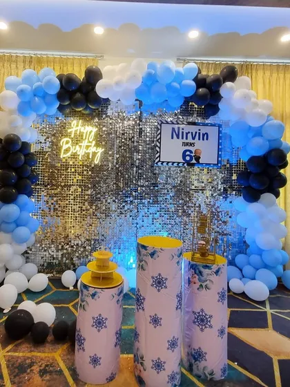 This Boss Baby theme for a 6th birthday features a silver sequin wall backdrop. The setup is framed by a blue, black, and white balloon arch and includes themed cake stands, making it a cool and fun party design.