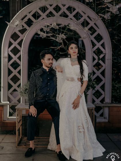 A stylish, full-length portrait of the couple at their Sangeet, showcasing their elegant white outfits.