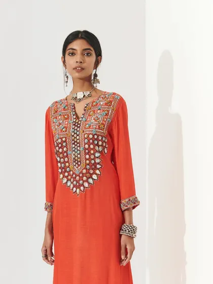 A model in a vibrant orange embroidered kurta. The makeup is clean and bright, with a defined eye and a flawless complexion that makes the entire look pop.