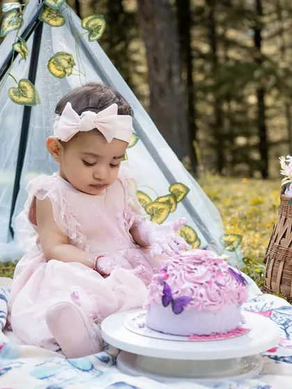 A close-up of the birthday girl intently focused on her cake. The details of the picnic blanket, basket of flowers, and her adorable pink dress add to the charm of this outdoor toddler portrait.