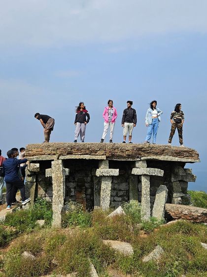 A group of friends posing on top of the stone structure at the Skandagiri summit.