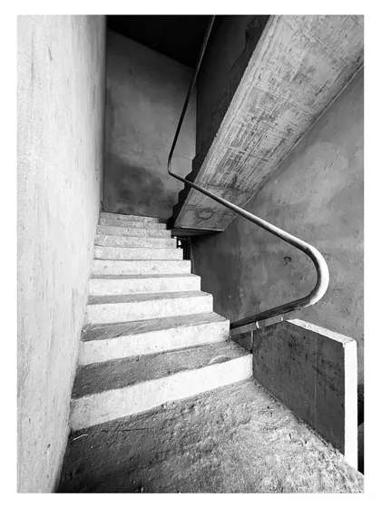 A detail of the curved concrete handrail as it navigates a turn in the staircase. The fluid form contrasts with the rough texture of the unfinished concrete.