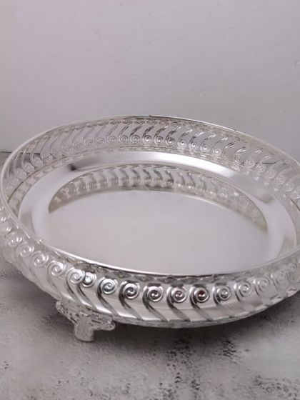 A German silver tray with a swirled pattern on the rim and small legs. It's a beautiful base for arranging pooja items.