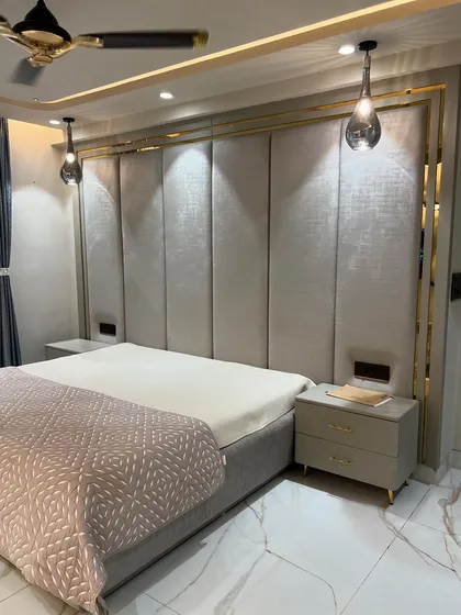 A master bedroom designed for rest and elegance. The custom-made upholstered headboard with gold metal inlay, combined with soft cove lighting and pendant lights, creates a sophisticated and serene environment.