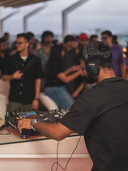 A view from behind the decks during a daytime event. You can see the relaxed crowd enjoying the music.