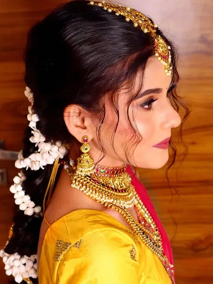 A side profile of a beautiful South Indian bridal look, showcasing the intricate braid adorned with mogra flowers and traditional hair accessories.