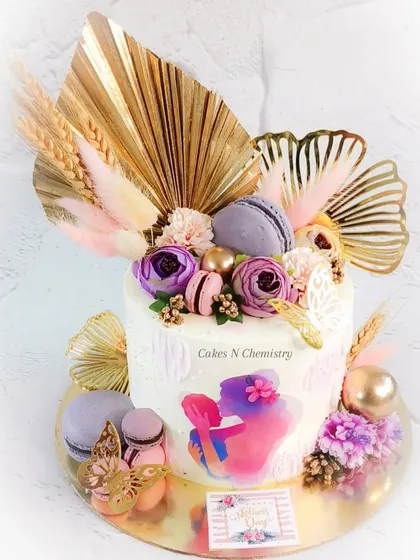 A beautiful cake designed for Mother's Day. This trendy cake is decorated with painted buttercream and adorned with modern toppers like golden palm leaves, gingko leaves, and macarons.