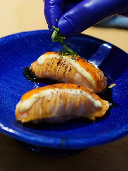 Our chef adds the finishing touch to a plate of Salmon Nigiri. A sprinkle of fresh herbs completes this dish of smoky, torched salmon perfection.