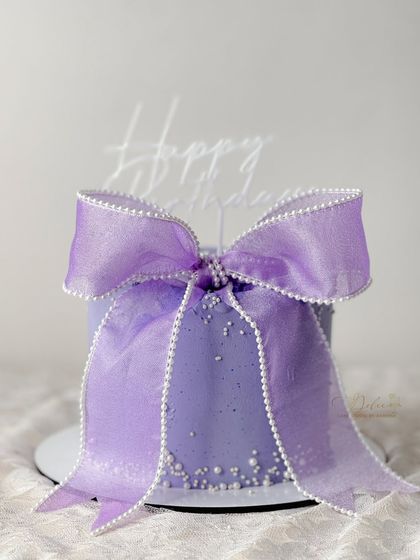 A lovely lavender-colored cake with a matching organza bow. The delicate pearl sprinkles add a touch of shimmer to this simple yet beautiful design.