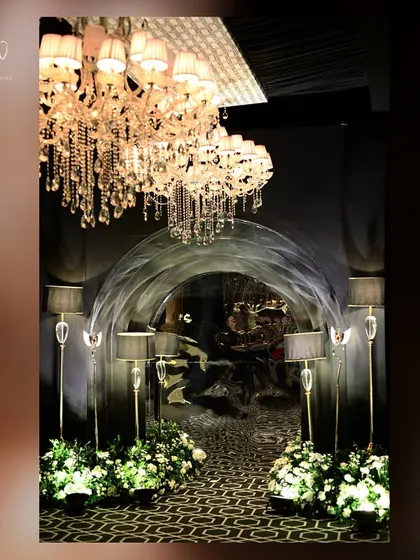 An entrance arch with a textured silver finish, flanked by elegant floor lamps and white floral arrangements.