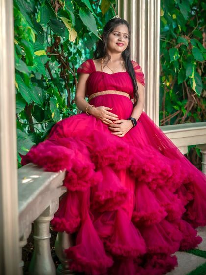 A stunning portrait of a mom-to-be in a tiered magenta gown. The lush green background makes the color pop, and the pose beautifully showcases the baby bump.