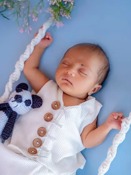 A sleeping newborn on a swing, accompanied by a tiny panda friend. This setup creates a sweet and peaceful image.