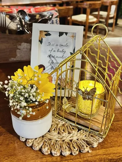 It's all about the little things. This charming centerpiece combines a miniature golden birdcage with a candle, fresh yellow flowers, and a framed quote, adding a touch of personalized sweetness to the guest tables.