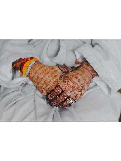 A close-up of the bride's hands, adorned with henna and traditional wedding bangles, resting in her lap. A quiet, detailed shot.