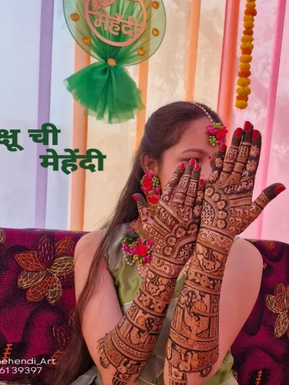A happy bride showing her full bridal mehendi, which features traditional bride and groom figures and extends all the way to her elbows.