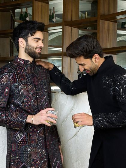 A moment of camaraderie, featuring two distinct yet complementary black kurtas. One is adorned with the hand-embroidered cheetah, the other with a complex, multi-hued pattern.
