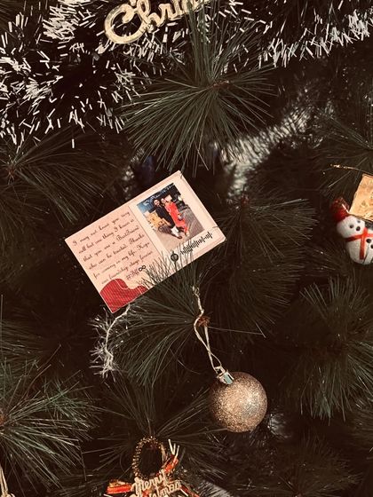 A custom Christmas card with a photo and message, shown hanging as an ornament on a tree.